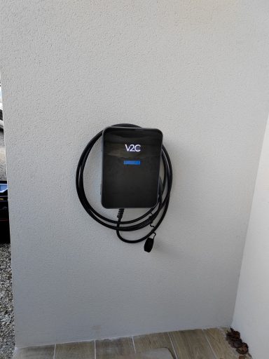 Chargeur mural noir avec câble accroché, fixé à un mur blanc.