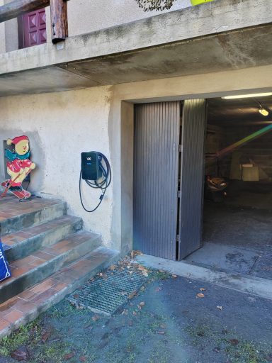 Porte ouverte sur un garage, escaliers sur le côté, téléphone mural à proximité.